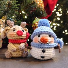 two crocheted snowmen sitting next to a christmas tree