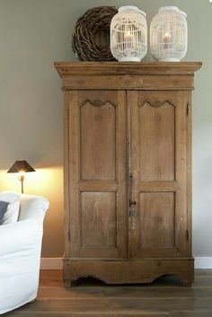 an old wooden cabinet with two birdcages on top and a white couch in the background