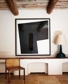 a chair sitting in front of a painting on the wall next to a table with a lamp