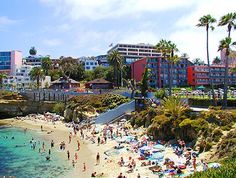 many people are on the beach and in the water near buildings with palm trees around them