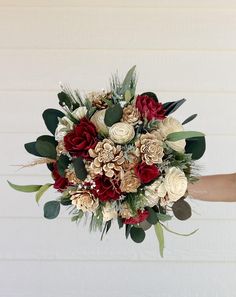 a bridal bouquet with red, white and green flowers is held by someone's hand