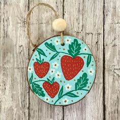 a ceramic ornament with strawberries and leaves painted on it, hanging from a rope