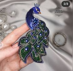 a woman's hand holding a peacock brooch with green and blue beads on it