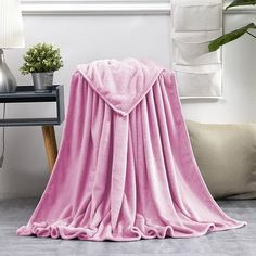 a pink blanket sitting on top of a wooden table next to a plant in a vase