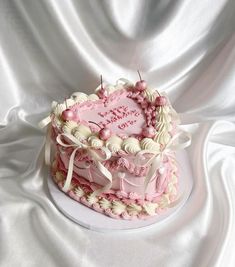 a heart shaped cake with pink icing and white decorations on top, sitting on a white cloth