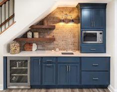 a kitchen with blue cabinets and white counter tops under a slanted ceiling that has stairs leading up to the second floor