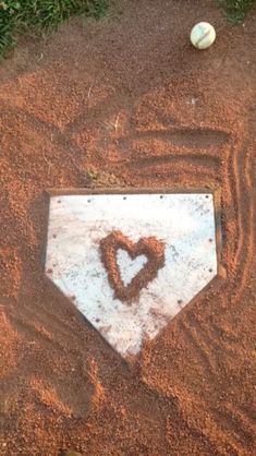 a baseball field with a heart drawn in the dirt and a ball on the ground