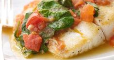 a white plate topped with fish covered in sauce and vegetables next to a knife and fork