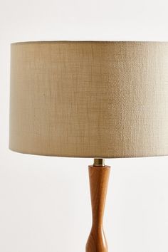 a wooden table lamp with a beige shade on it's base and a white wall in the background