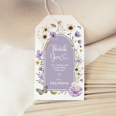 a thank you tag with purple flowers and butterflies is on top of a pile of folded books