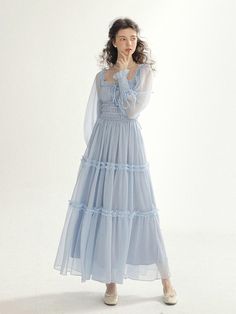 This product is an Isabel Smock Long Dress that exudes romantic elegance with its tiered tulle skirt and delicate smocking detail. The long sleeves are complemented by the smocked bodice, offering a snug fit with a vintage flair. This dress combines the airy lightness of the fabric with the intricate detail of the smocking, creating a harmonious blend of sophistication and whimsy. - The dress is adorned with tiered tulle layers, each accented with a ruffle trim, adding dimension and a fairy-tale quality.- Its smocked bodice provides both comfort and a tailored appearance, enhancing the dress's feminine appeal.- The long, sheer sleeves offer coverage while maintaining the dress's ethereal aesthetic.- Crafted for those special occasions, the Isabel Smock Long Dress is a beautiful choice Light Blue Cottagecore Dress, Ethereal Dress Casual, Feminine Long Sleeve Dress With Smocked Bodice, Feminine Long Sleeve Smocked Dress With Smocked Bodice, Feminine Long Sleeve Smocked Dress, Feminine Long Sleeve Smocked Ruched Dress, Feminine Long Sleeve Ruched Smocked Dress, Feminine Smocked Dress With Ruffles And Tiered Skirt, Feminine Tiered Skirt Smocked Dress With Ruffles