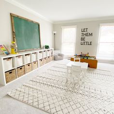 a living room with white furniture and a chalkboard on the wall above it that says let them be little