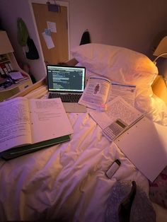 an open laptop computer sitting on top of a bed next to notebooks and papers