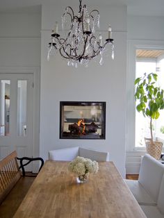 a dining room table with chairs and a chandelier hanging from the ceiling in front of a fireplace