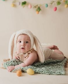 a baby wearing a bunny hat laying on top of a blanket next to an easter decoration