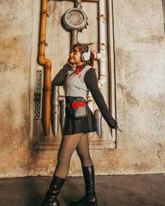 a woman in tights and boots standing next to a wall with pipes on it