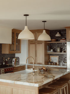 a kitchen with wooden cabinets and white marble counter tops, two pendant lights over the island