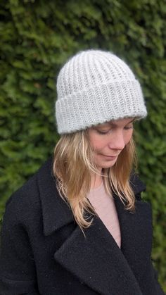 a woman wearing a white knitted hat while looking at her cell phone in front of some bushes