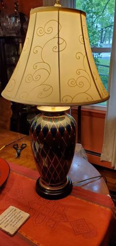 a lamp sitting on top of a table next to a book and glass vase with writing on it