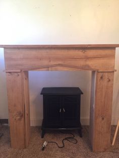 a small black cabinet sitting under a wooden fireplace mantel in a room with carpeted flooring