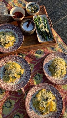 four plates with different types of food on them sitting on a colorful table cloth next to glasses and water