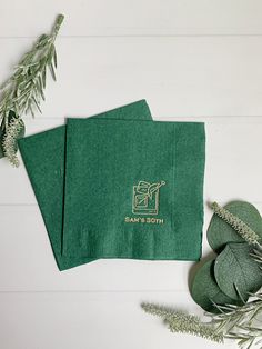 two green napkins sitting on top of each other next to some plants and leaves