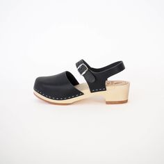 Discover The Charlie Clog, our contemporary twist inspired by the classic Mary Jane. This timeless closed-toe, design features an adjustable back strap and boasts the broadest toe among our closed-toe styles. Whether worn barefoot or paired with socks or tights of any thickness, The Charlie is versatile. The low heel option caters to those with flatter feet or a preference for comfort in daily wear, while the high base style introduces a modern and slightly more dressy option. Both base choices Modern Clogs With Rubber Sole And Open Heel, Modern Open Heel Clogs With Rubber Sole, Modern Closed Toe Clogs With Stacked Heel, Modern Closed Toe Clogs With Buckle Closure, Black Clogs With Ankle Strap And Leather Sole, Black Ankle Strap Clogs With Leather Sole, Modern Sandals With Wooden Heel And Closed Toe, American Midwest, Low Heel Sandals