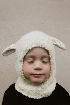 a young boy wearing a sheep hat and black shirt with his eyes closed while standing in front of a wall