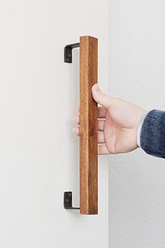 a person holding onto a wooden handle on a white wall with a black door frame