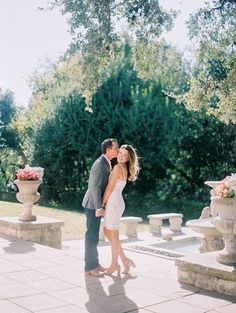 a man and woman are kissing in front of some stone urns with flowers on them