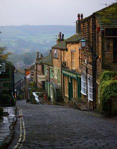 a cobblestone street with buildings on both sides and hills in the distance behind it