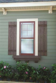 a house with green siding and brown shutters on the windowsill, along with pink flowers