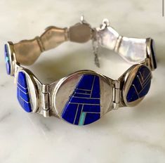 Amazing lapis inlay bracelet.Own this museum quality Canyon Collection work of art ,handcrafted and signed by Rick Tolino and Zora Joe.Unique contemporary design with different sized links of lapis inlay with an accent of turquoise.Secure lock with safety chain link. Size 7 7/8 inch length Largest link is 1 × 1 inch,smallest 1/2 inch Weight 51.3 Grams Stamped Sterling Hallmark Rick Tolino and Zora Joe New,never worn, from vintage 1980's collection. Lapis Earrings, Turquoise Earrings Dangle, Navajo Turquoise, Safety Chain, Buffalo Ny, Lovely Earrings, Lovely Jewellery, Earrings Photo, Turquoise Earrings