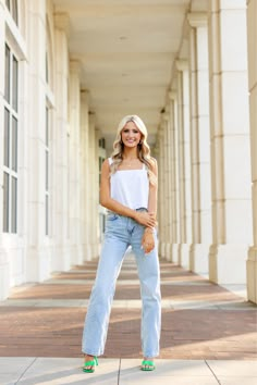 a woman standing on the sidewalk wearing high rise jeans and a white tank top with green shoes