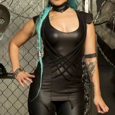 a woman with blue hair wearing black leather clothes and chains on her neck, standing in front of a chain fence