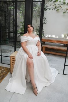 a woman in a white dress is sitting on a bench and posing for the camera