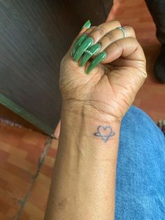 a woman's arm with a green manicure on it and a heart tattoo