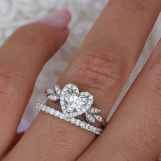 a woman's hand with two wedding rings on top of her finger and the ring has an oval shaped diamond surrounded by smaller round diamonds