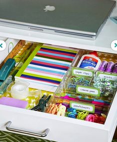 an open drawer with craft supplies and a laptop on the table in front of it