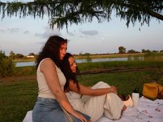 two women sitting on a blanket under a tree