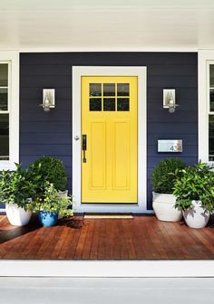 two potted plants sit on the front porch of a blue and white house with yellow door