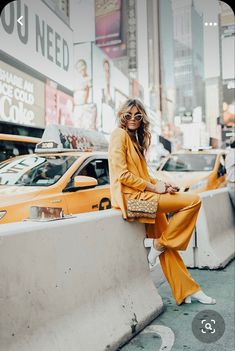 a woman sitting on the side of a wall next to taxi cabs in new york city