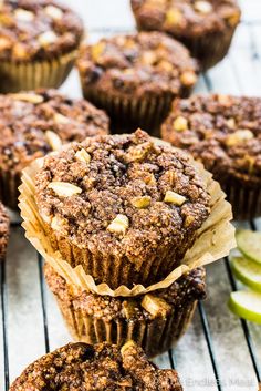 some muffins are stacked on top of each other with apples in the background