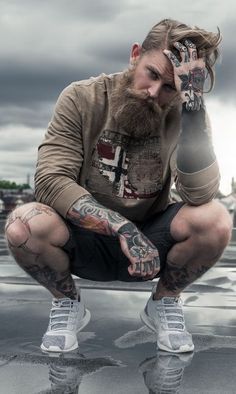 a man with tattoos squatting down on the ground and holding his hands to his face