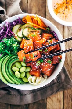 a white bowl filled with vegetables and chopsticks on top of a wooden table