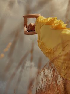 a woman in a yellow dress is posing for the camera with her arms behind her head