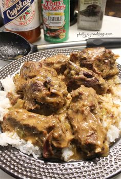 meat and gravy served over rice on a plate with beer bottles in the background