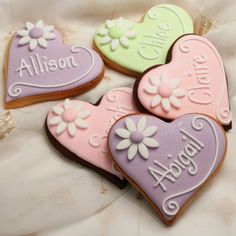 four decorated heart shaped cookies with names and hearts on them, all in pastel colors