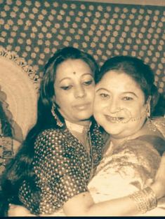 an old photo of two women hugging each other on a couch with decorative wallpaper behind them