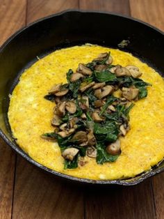 an omelet with spinach and mushrooms in a skillet on a wooden table